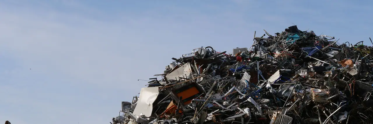 A large stockpile of mixed scrap metal rising against an open sky, light iron, appliance shells and cut sections tipped together.