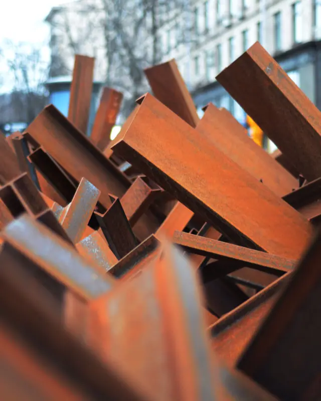 Cut lengths of weathered structural steel stacked at an angle: I-beams, channel and angle iron taken out of a building.